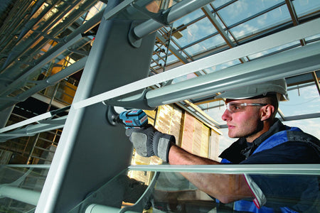 A worker uses the compact Bosch 12V impact driver to fasten a bracket in a tight space between metal framing.