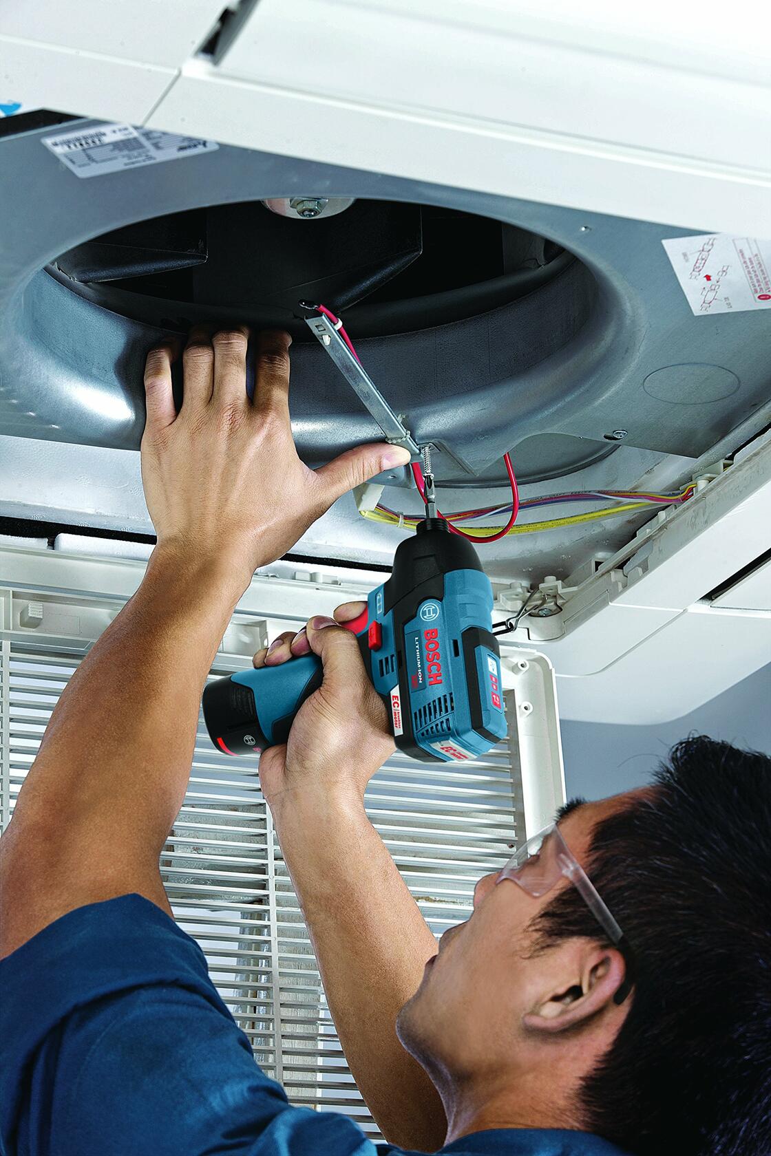 A technician uses the Bosch 12V impact driver to work on the inside of a ceiling-mounted air conditioning unit.