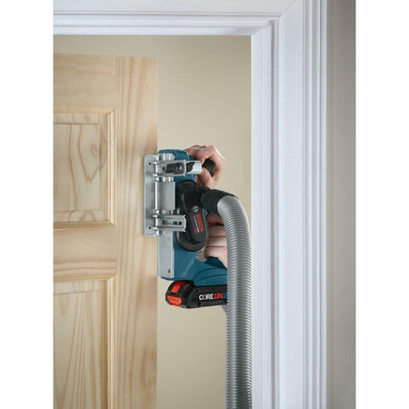 The Bosch cordless planer being used to trim the edge of a wooden door, demonstrating its use for door hanging and fitting.