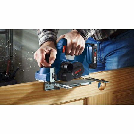A close-up view of the Bosch cordless planer with its edge guide attached, being used to smooth the edge of a wooden door."