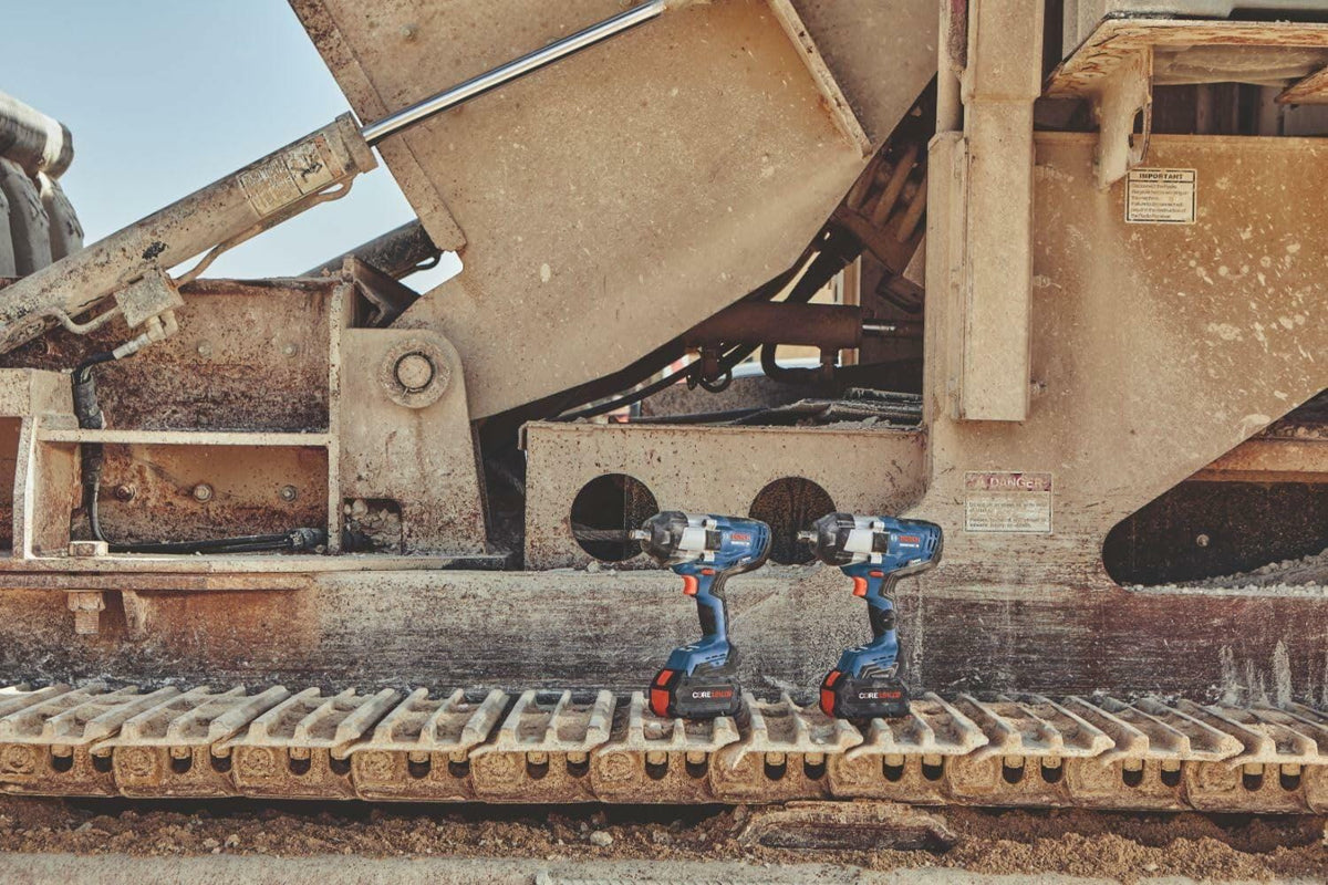 Two Bosch PROFACTOR impact wrenches sitting on the dirty tracks of a piece of heavy construction machinery on a jobsite.