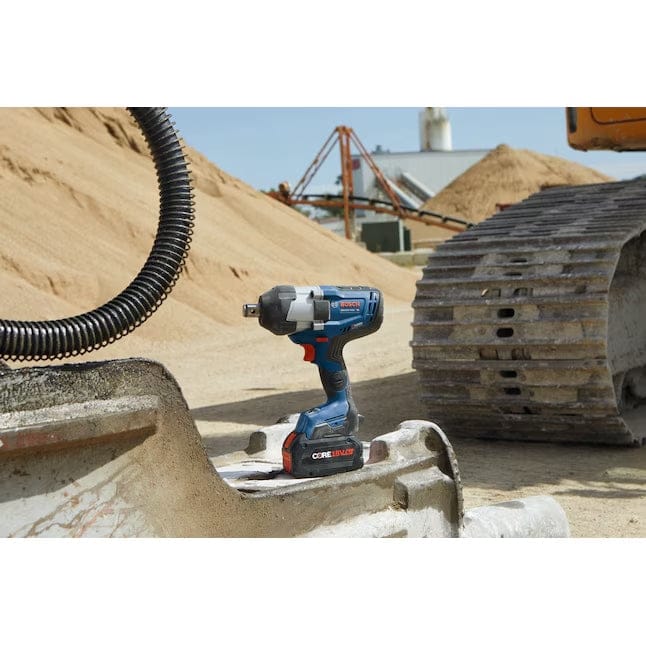 The Bosch GDS18V-770CN impact wrench with a CORE18V battery is shown resting on a concrete form at a construction site, with sand piles and heavy equipment in the background.