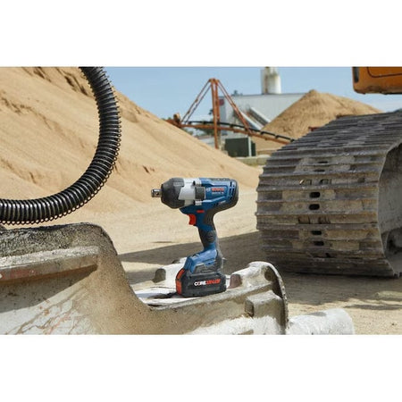 The Bosch GDS18V-770CN impact wrench with a CORE18V battery is shown resting on a concrete form at a construction site, with sand piles and heavy equipment in the background.