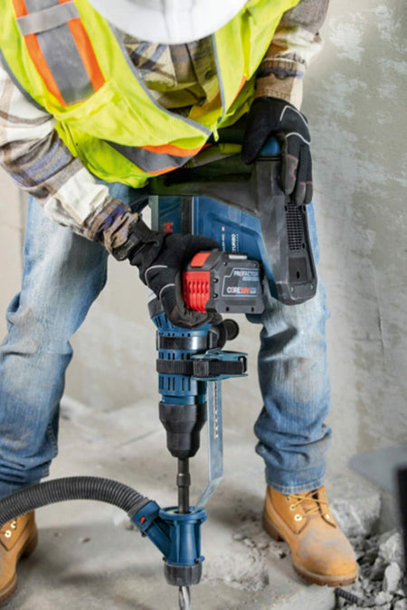 A worker uses the Bosch rotary hammer with a chisel bit and an attached dust extraction system to chip away at a concrete surface.