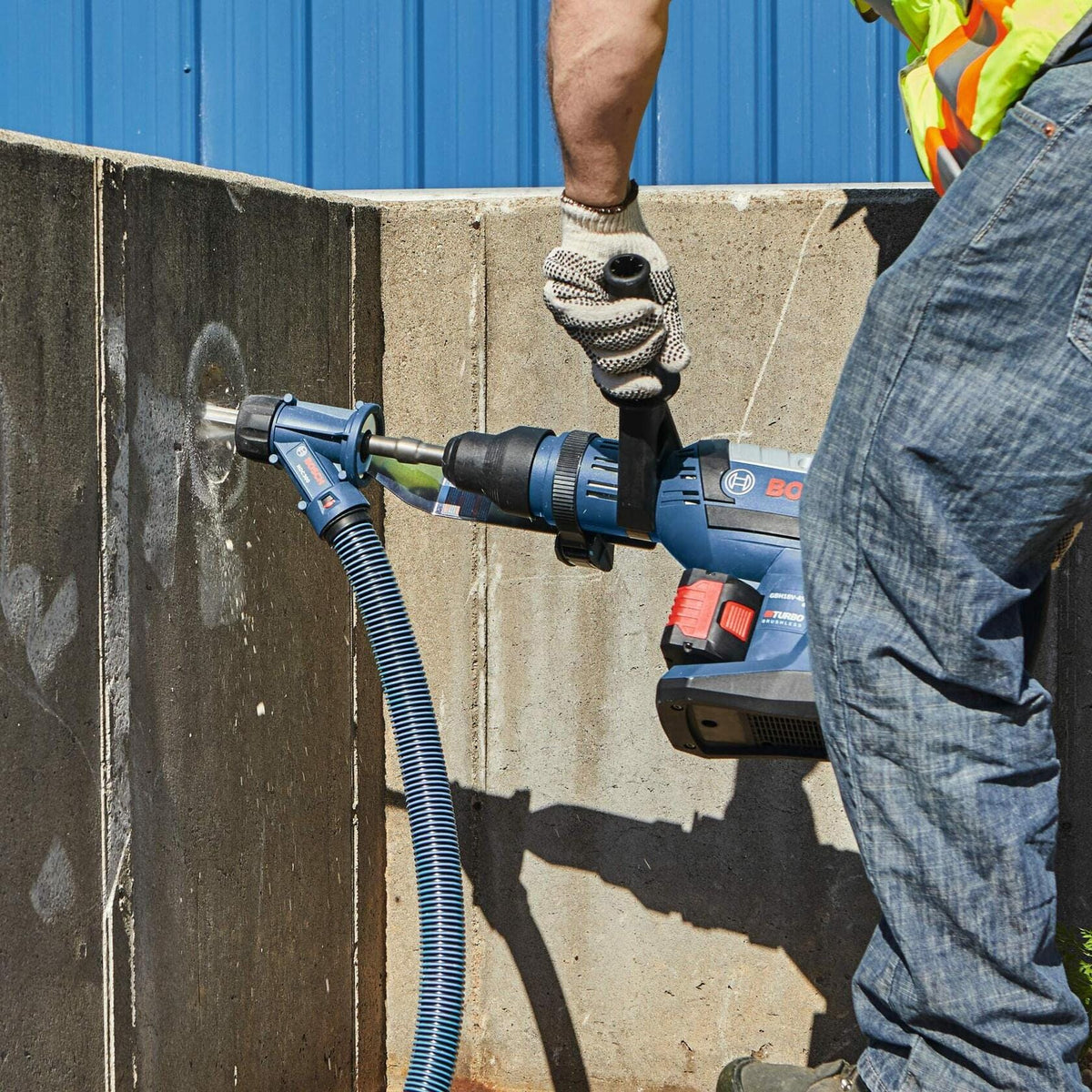 A worker holds the Bosch rotary hammer horizontally to drill into a concrete wall, with a dust collection attachment connected to a vacuum hose.