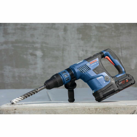 The Bosch PROFACTOR rotary hammer with a large carbide drill bit inserted, resting on a concrete block on a jobsite.