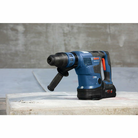 The Bosch PROFACTOR rotary hammer resting on a concrete surface in front of a concrete wall at a construction site.