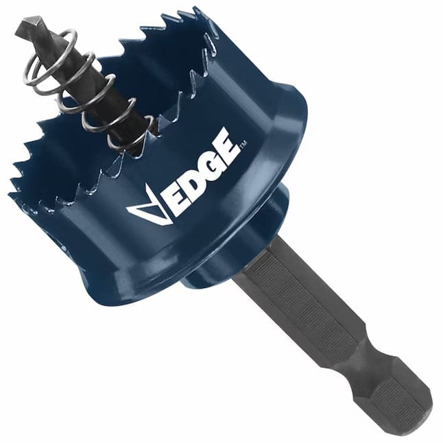 This is an image of a hole saw, a circular saw blade used for cutting large holes, with a dark blue body and jagged teeth around its circumference. A black hexagonal shaft extends diagonally from the saw's base, with a smaller drill bit and a coiled spring positioned inside the hollow center, designed to guide the tool while cutting.