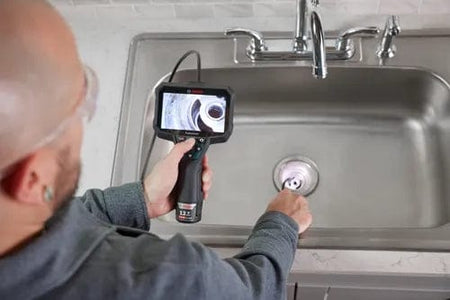 Bosch inspection camera inserted into sink drain; screen displays live feed of pipe structure during plumbing check.
