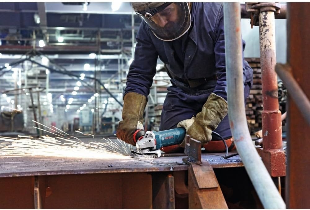 Worker in protective gear using an angle grinder in an industrial workshop, with sparks flying from metal surface during active grinding