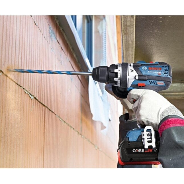 Person drilling into a brick wall with Bosch CORE18V cordless drill and long masonry bit, wearing gloves in a construction setting.