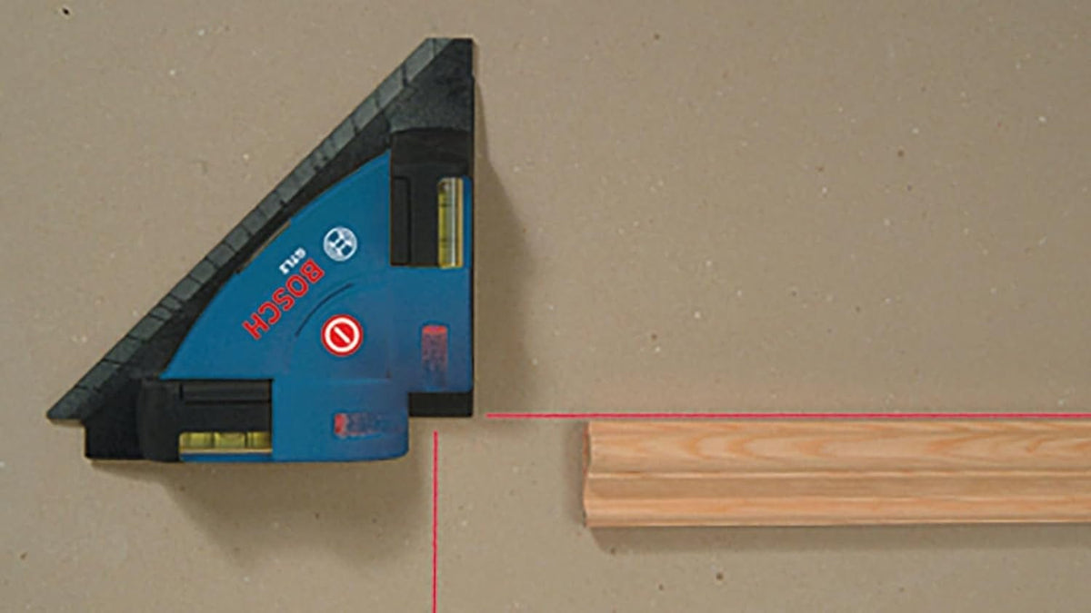 Bosch GTL2 laser level tool emitting two red laser lines at a right angle, used to align a wood piece on a flat surface with built-in bubble levels