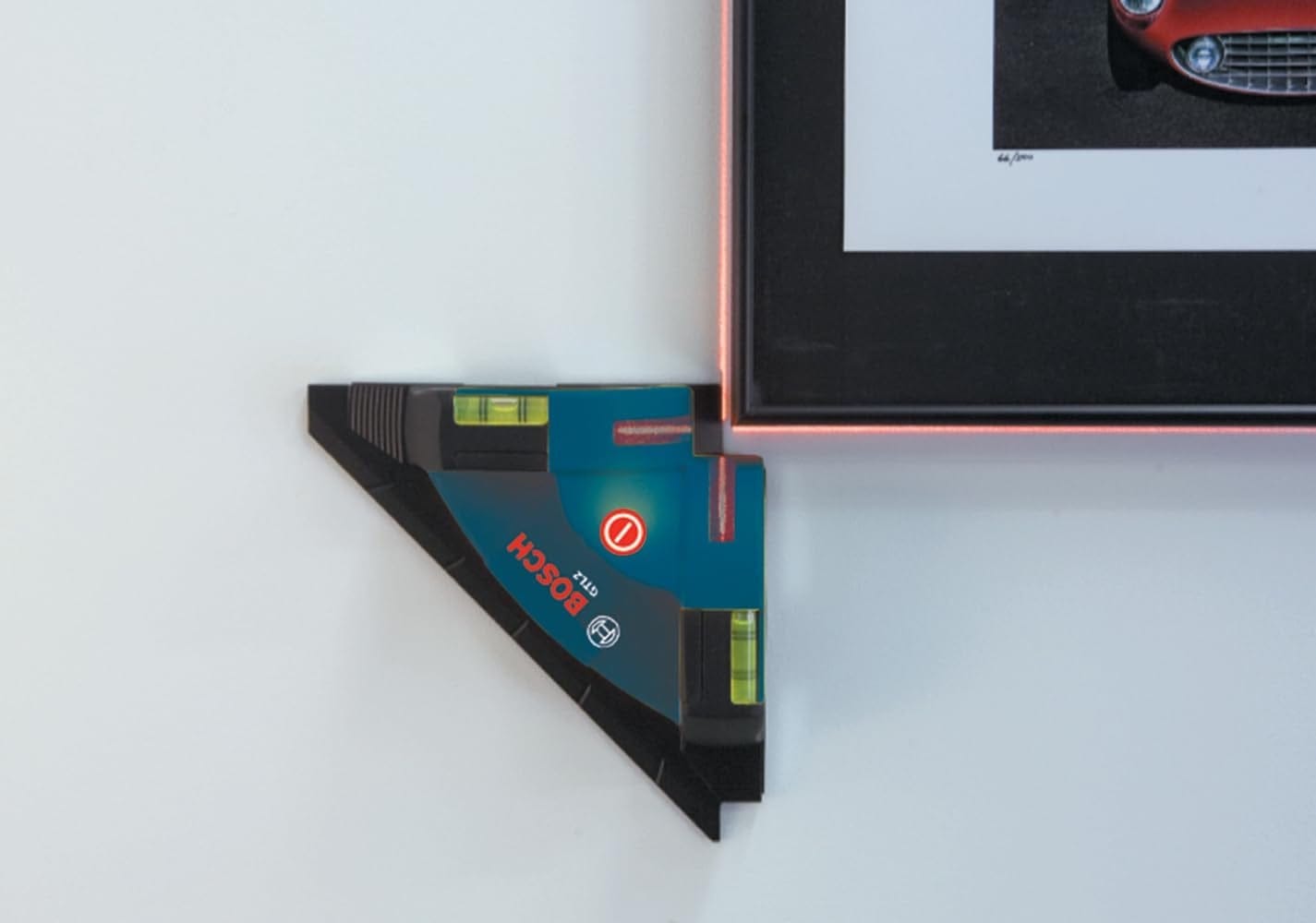 Bosch digital angle finder checking the alignment of a picture frame on a wall, with bubble levels and digital display showing the angle is not level.