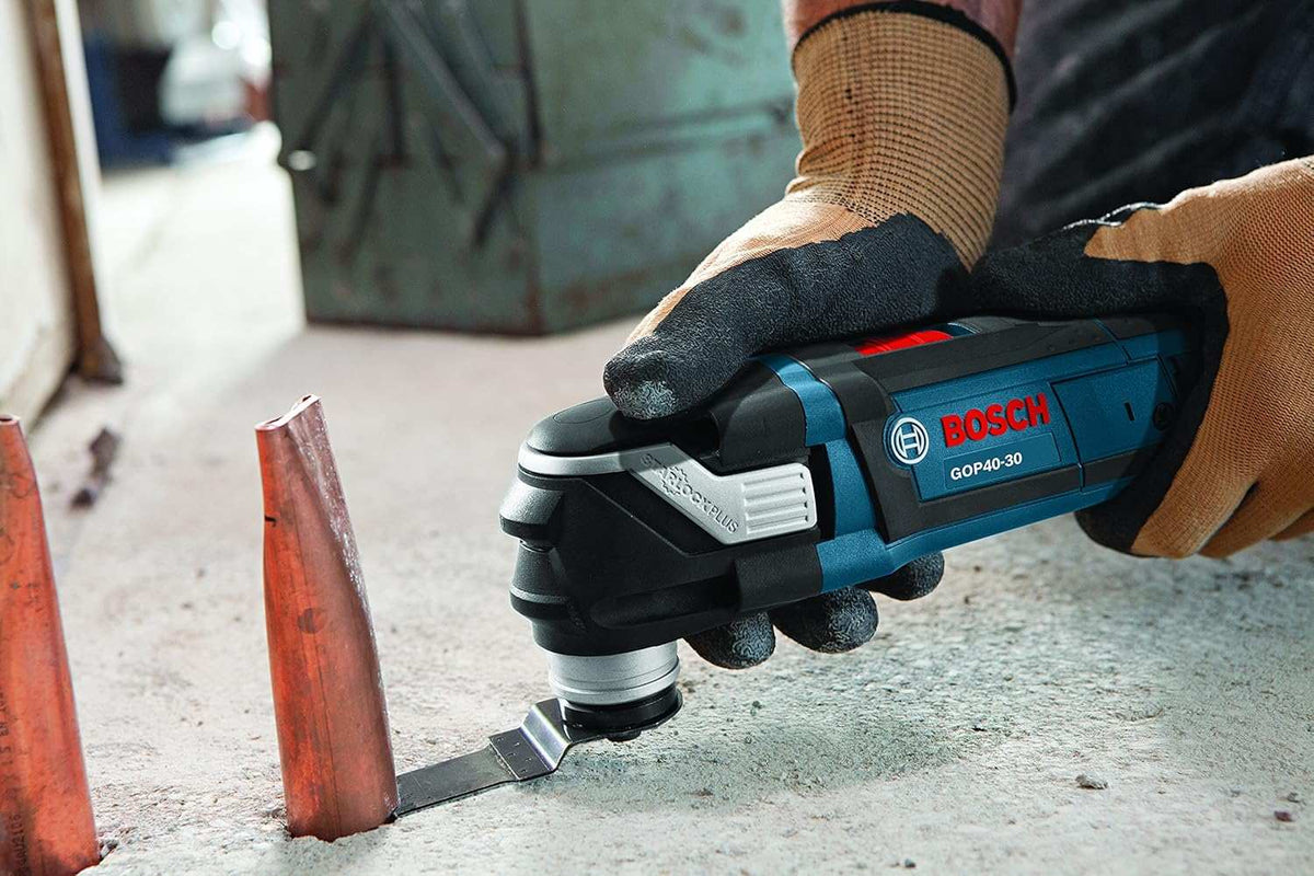 Close-up of Bosch GOP40-30 multi-tool cutting a copper pipe on a concrete surface, showing precision metal cutting in a construction setting