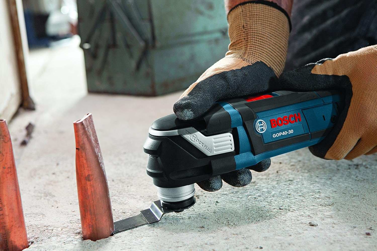 Close-up of Bosch GOP40-30 multi-tool cutting a copper pipe on a concrete surface, showing precision metal cutting in a construction setting
