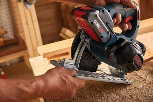 Person using Bosch circular saw with CORE18V battery to cut wood on a workbench, adjusting the base plate while wearing gloves.