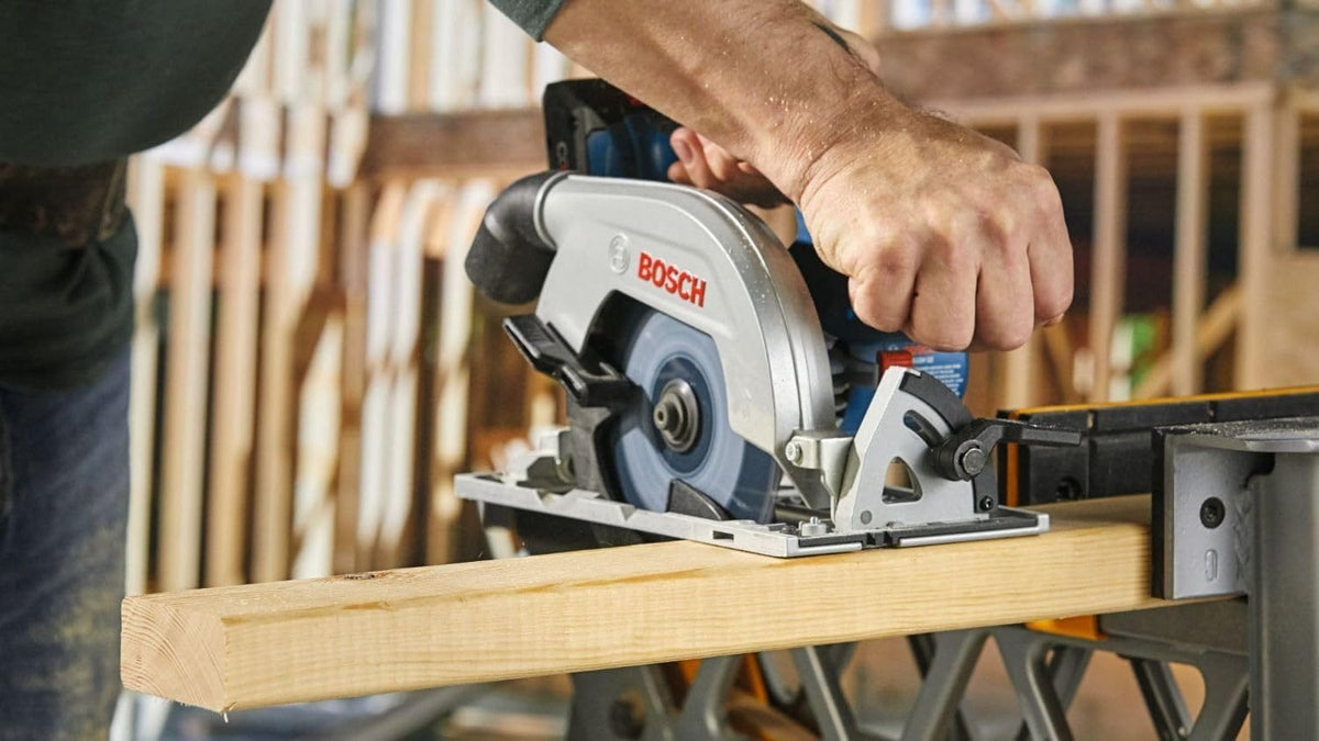Person using Bosch circular saw on a workbench to cut wood, gripping the saw with both hands in a construction or workshop setting