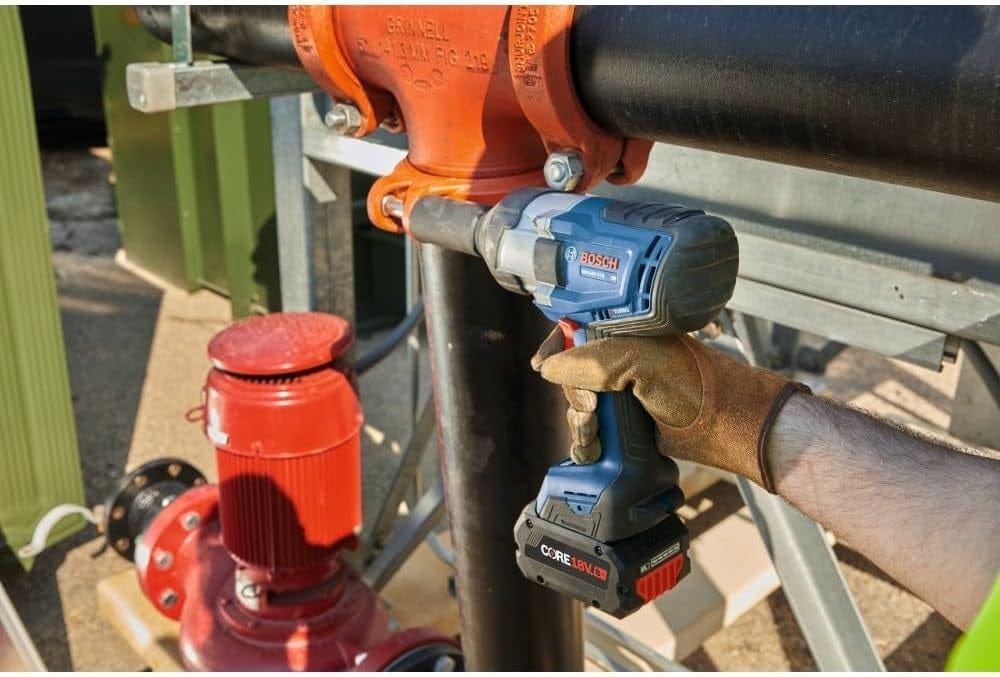Person using Bosch impact wrench to tighten bolts on a black pipe with orange flange labeled “GRINNELL FIG 705” in an industrial settin