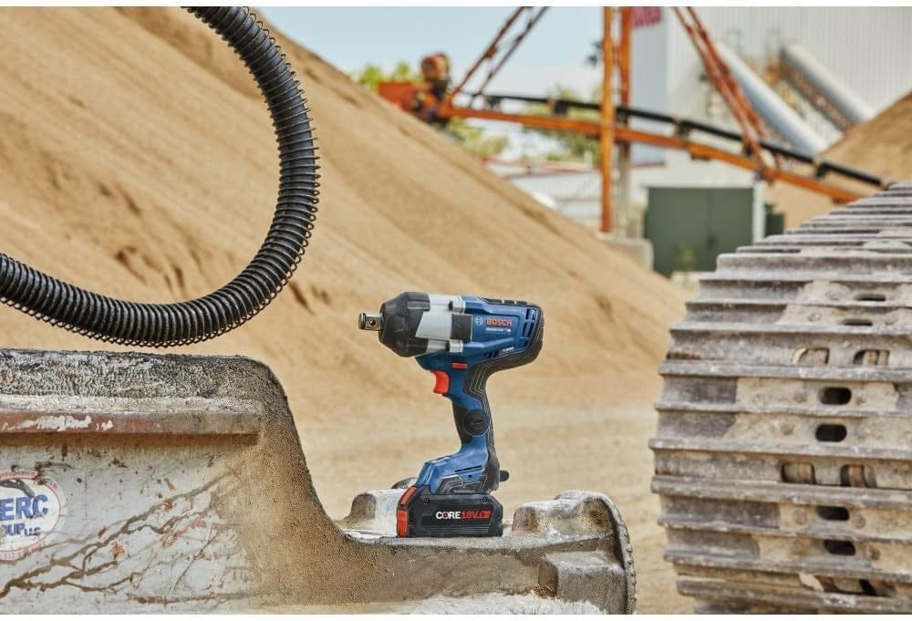 Bosch cordless impact wrench placed on heavy construction equipment at a jobsite, surrounded by sand piles and industrial machinery.
