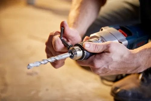 A person uses a chuck key to secure a drill bit into the Bosch HD18-2 hammer drill.