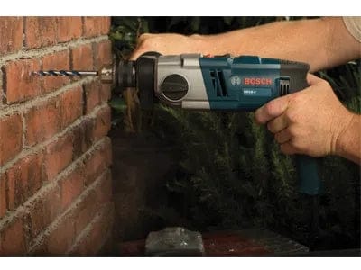 A person using the Bosch HD18-2 hammer drill to drill a hole into a red brick wall.