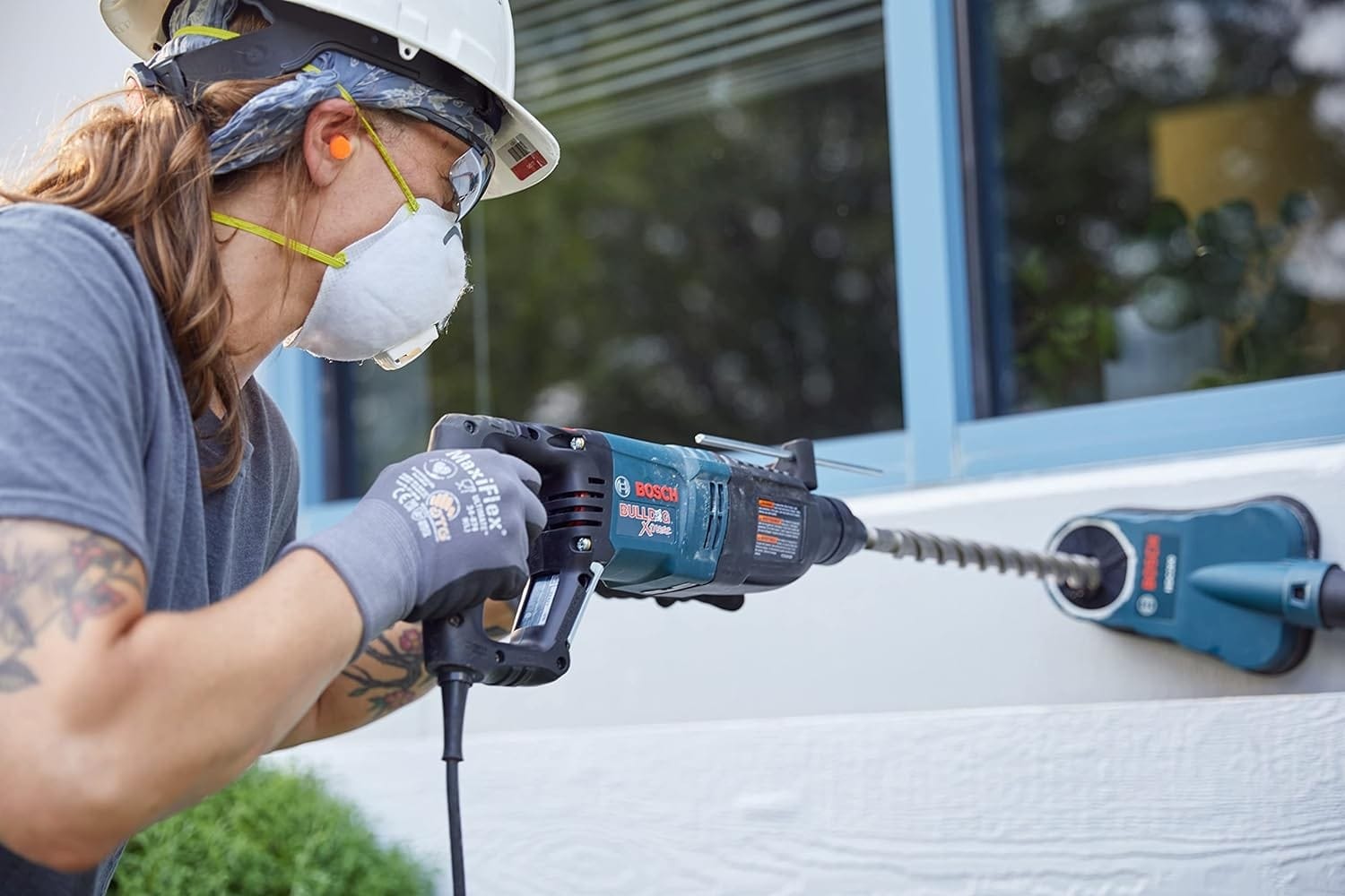 A profile view of a worker drilling into a wall using the rotary hammer connected to a dust collection attachment to maintain a clean work environment.
