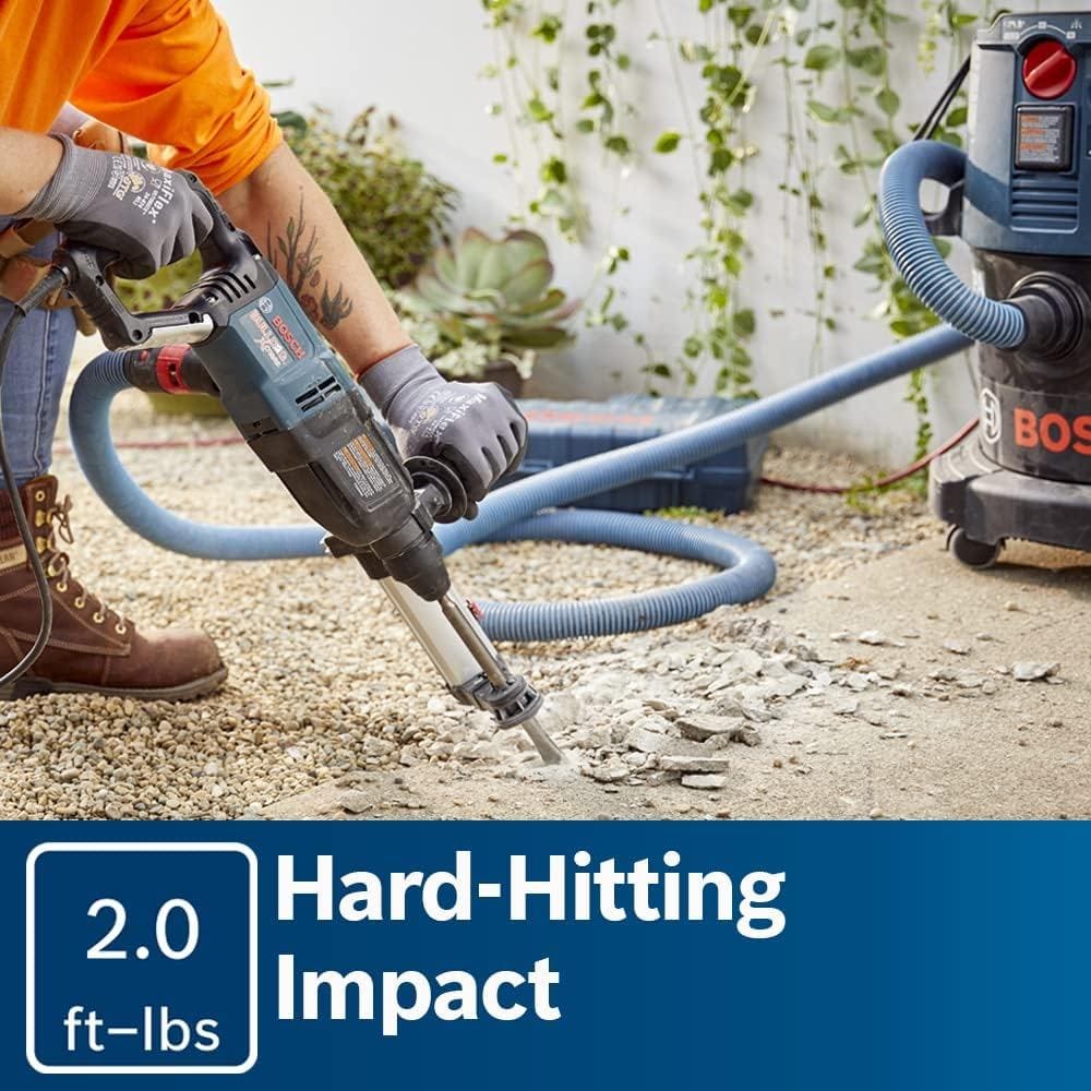 An action shot of a worker using the rotary hammer to chip up concrete flooring, connected to a dust extraction attachment and vacuum for a clean workspace.