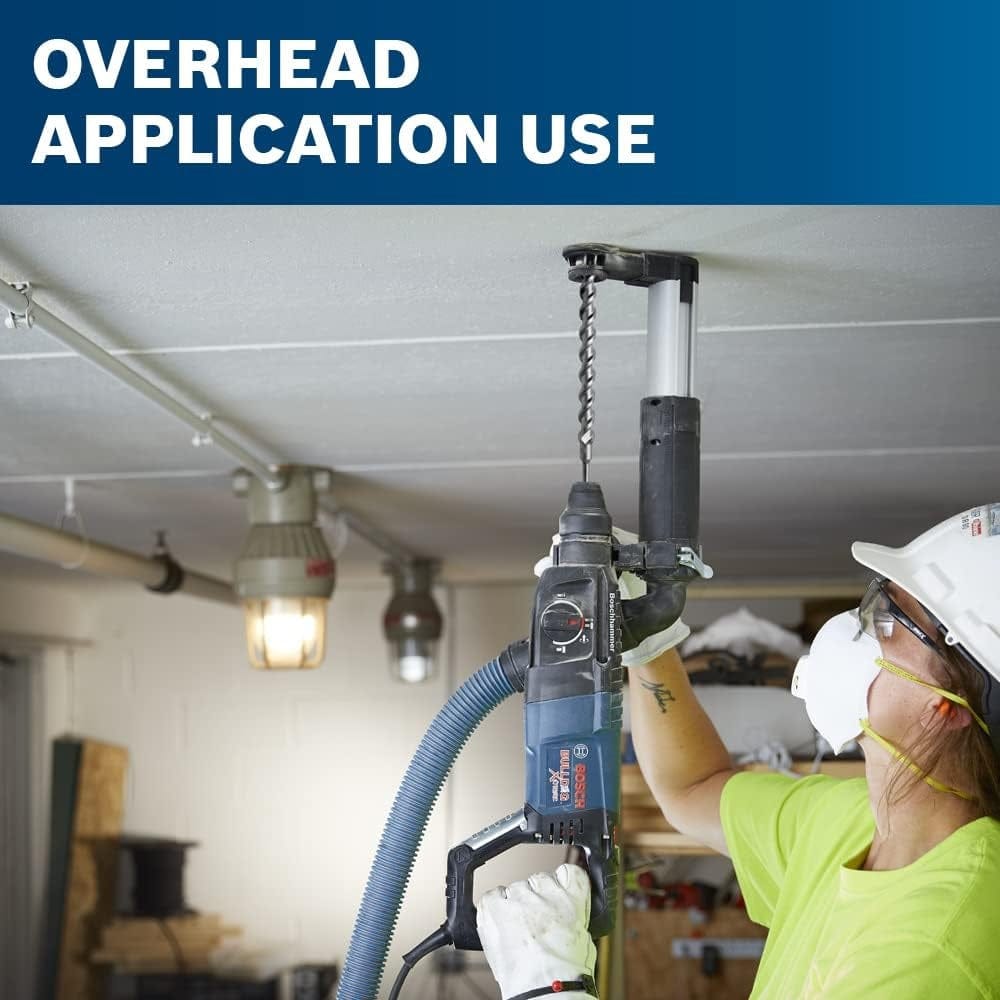 A construction worker wearing a hard hat using the rotary hammer overhead to drill into a concrete ceiling, utilizing a dust collection attachment to capture debris.