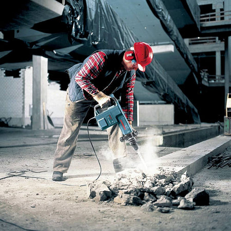 An operator in a hard hat and safety gear uses the Bosch 11316EVS-46 demolition hammer to break up a concrete slab on an industrial job site.