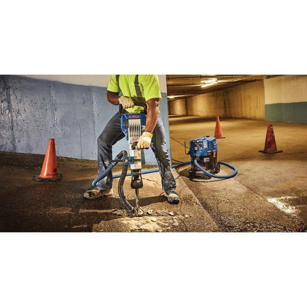 A person using the Bosch breaker hammer with a dust extraction attachment to demolish a concrete floor in an indoor garage.