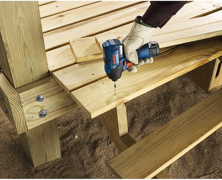 A gloved hand using the Bosch PS42N impact driver to fasten wooden planks on an outdoor deck construction project.