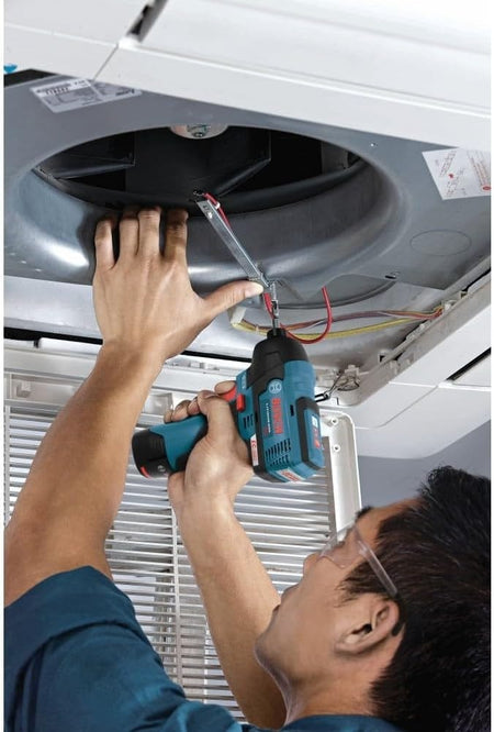 A technician reaching overhead to use the compact Bosch PS42N impact driver on an HVAC unit, demonstrating its utility in tight spaces.