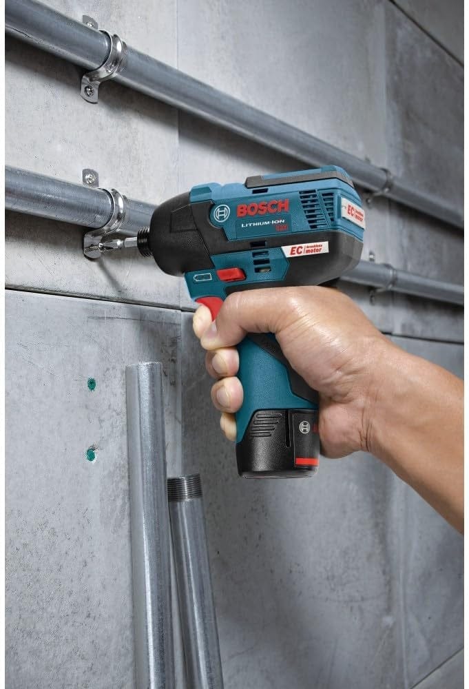A close-up of a hand using the Bosch PS42N impact driver to secure a metal pipe clamp to a concrete wall.