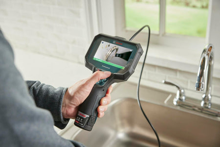 A person holds the Bosch inspection camera over a kitchen sink, and the screen displays a "File saved" confirmation after capturing an image of a ring lost in the drain.
