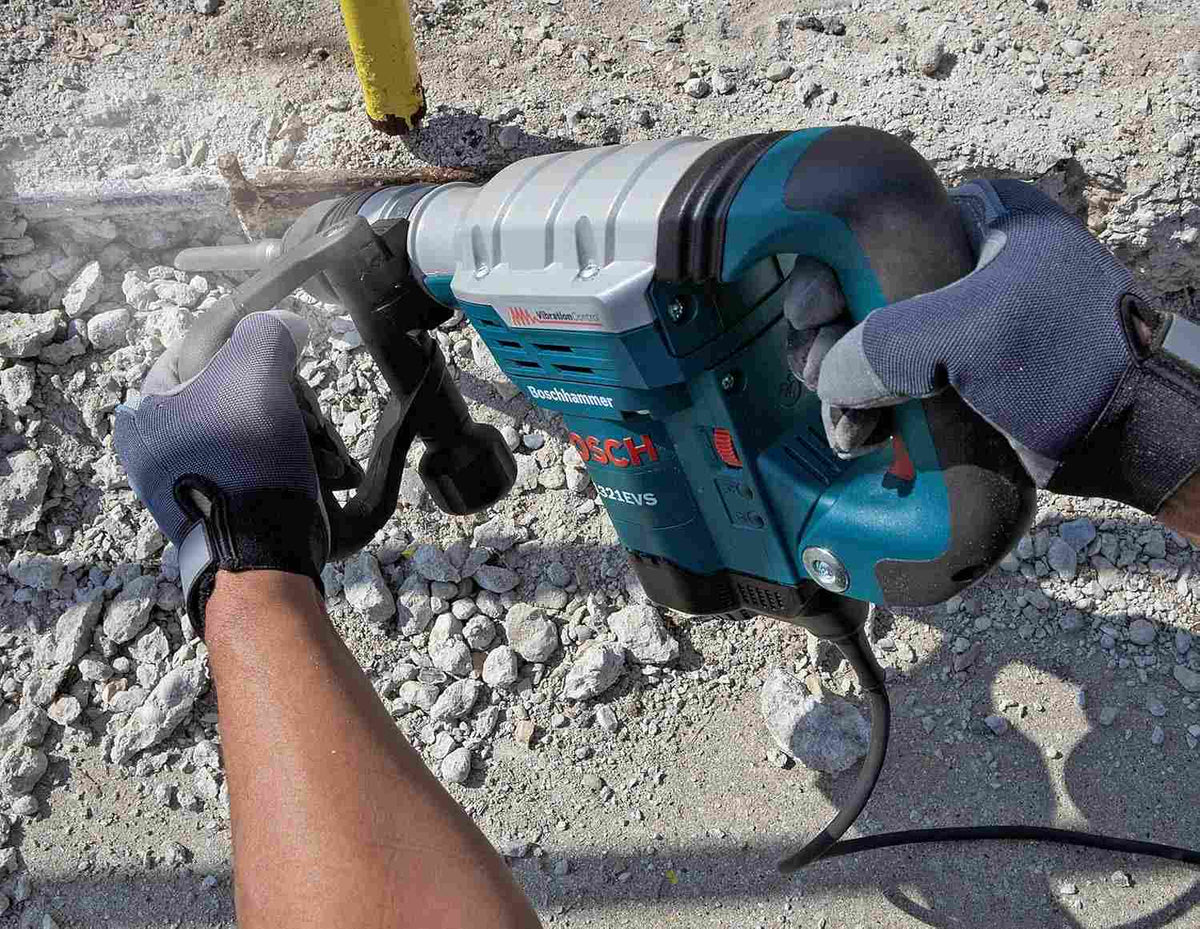 A close-up action shot of a worker's gloved hands holding the Bosch 11321EVS to break up concrete rubble on the ground.
