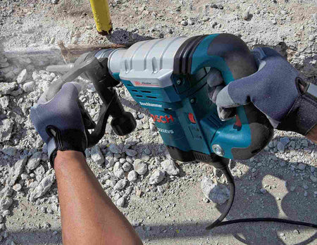 A close-up action shot of a worker's gloved hands holding the Bosch 11321EVS to break up concrete rubble on the ground.