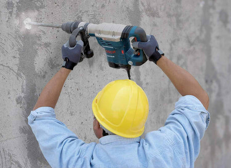 An over-the-shoulder view of a worker holding the Bosch 11321EVS hammer upward to chisel a hole in a concrete wall.