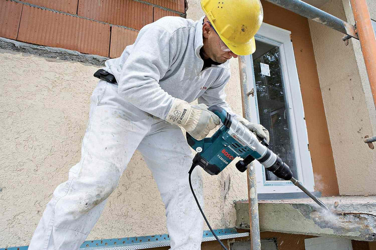 A worker in full safety gear uses the Bosch 11321EVS demolition hammer to break up a concrete ledge on an exterior wall.