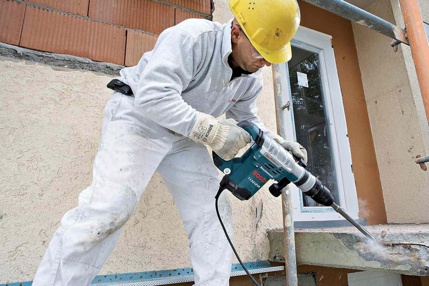A worker in full safety gear uses the Bosch 11321EVS demolition hammer to break up a concrete ledge on an exterior wall.