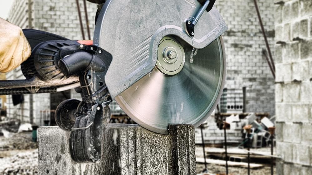 Construction worker using a high-speed circular saw with water cooling to cut a concrete block at a job site, demonstrating the blade’s wet cutting capability and power.