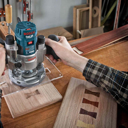 High angle action shot of a woodworker using a router with a template to cut joinery into a piece of wood.