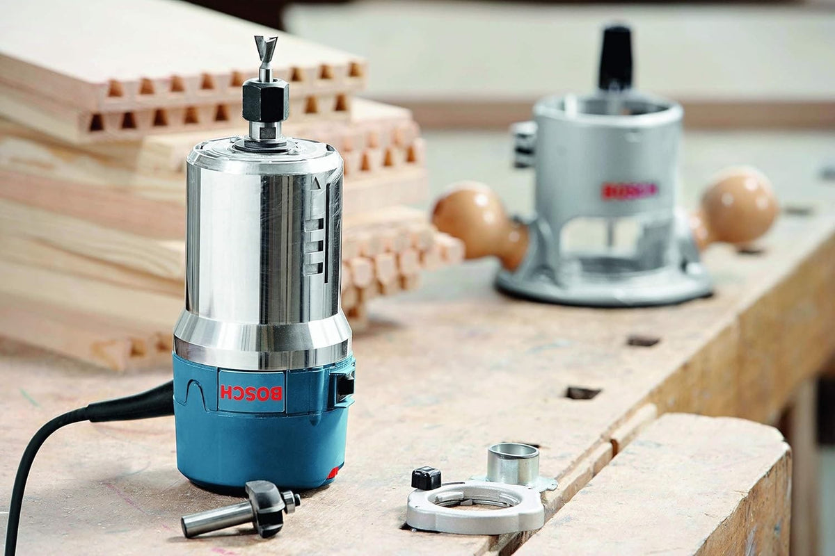 Studio shot of the Bosch 1617EVS motor unit removed from the fixed base, shown next to router bits and template guides on a professional woodworking bench.
