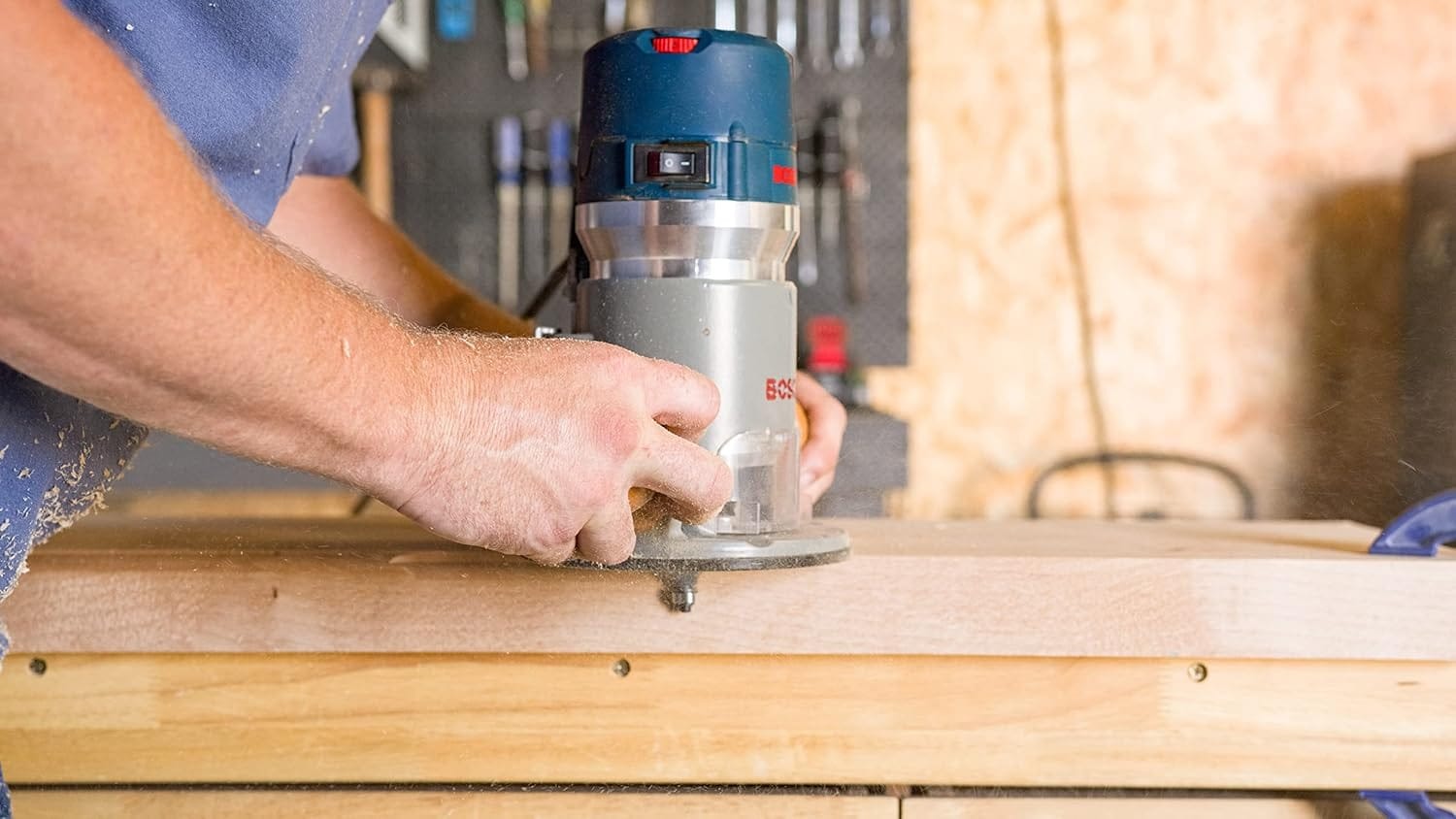 Side action view of the Bosch fixed-base router in operation on a workbench, highlighting the dust-sealed power switch and smooth glide across a hardwood surface.
