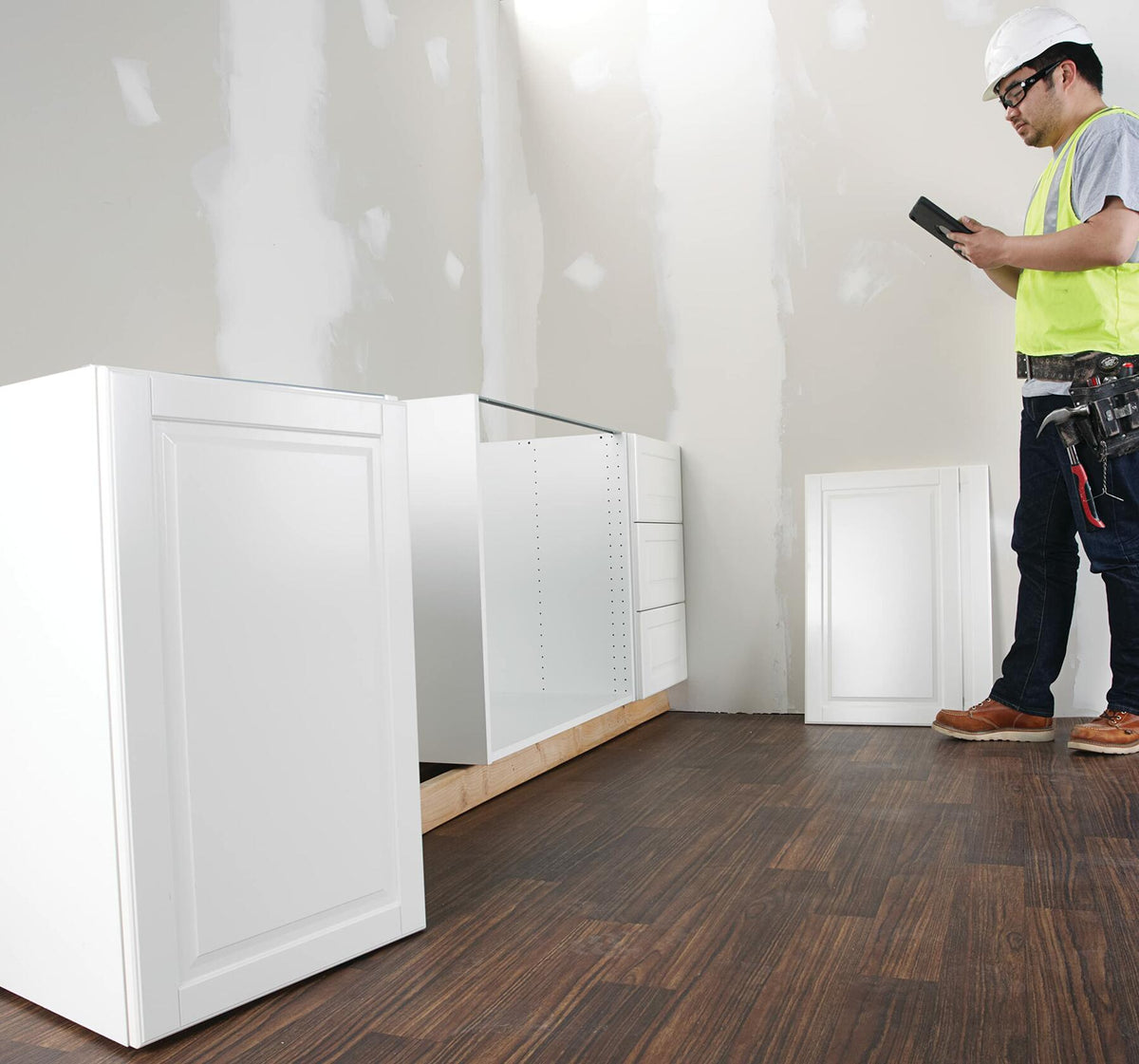 Construction worker standing next to installed base cabinets, reviewing measurements and floor plans on a digital tablet using the Bosch MeasureOn app