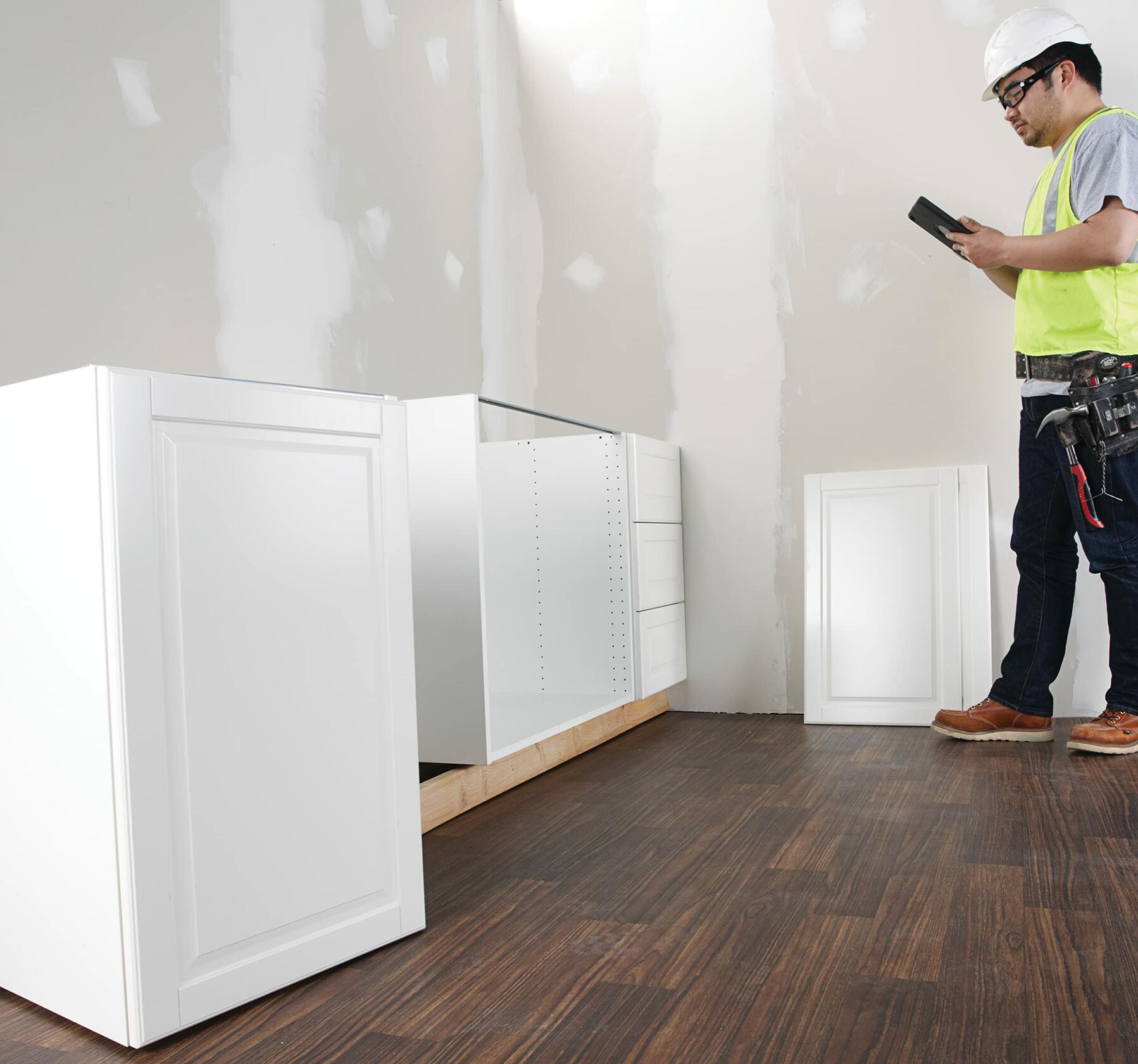 Construction worker standing next to installed base cabinets, reviewing measurements and floor plans on a digital tablet using the Bosch MeasureOn app