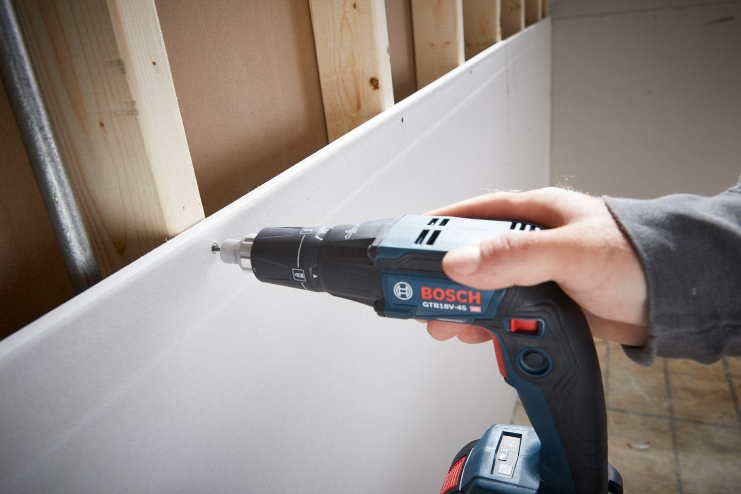 A person holds the Bosch GTB18V-45 screwgun and uses it to drive a screw into a sheet of drywall attached to wooden studs.
