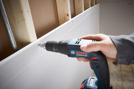 A person holds the Bosch GTB18V-45 screwgun and uses it to drive a screw into a sheet of drywall attached to wooden studs.