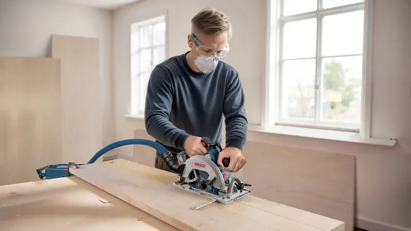 A woodworker wearing a protective face mask, safety glasses, and earplugs guides the Bosch 7-1/4 inch circular saw through a long piece of lumber. The operator utilizes an attached adjustable metal guide rail accessory to maintain a highly straight, precise rip cut path down the board.
