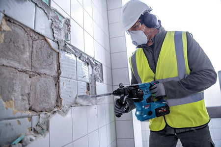 An action shot of a worker in full safety gear using the Bosch GBH18V-28C cordless rotary hammer, in hammer-only mode, to chisel and remove old wall tiles.