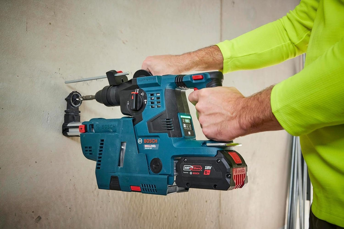 An action shot of a worker in a bright green vest using the Bosch GBH18V-28C cordless rotary hammer with a dust extraction attachment to drill horizontally into a concrete wall.